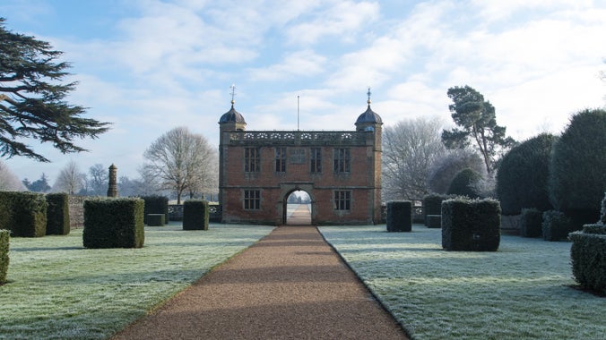 A view of the courtyard and Tudor Gatehouse taking centre stage, framed by frosty lawns and dark topiary, against a wintry, blue sky.